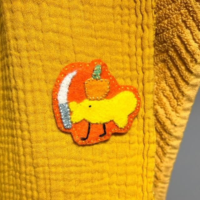 photo of final pin, of a yellow fish with legs, holding a curved knife in their lips and a little pumpkin on their head. the elements are all made in felt and sewn to an orange background