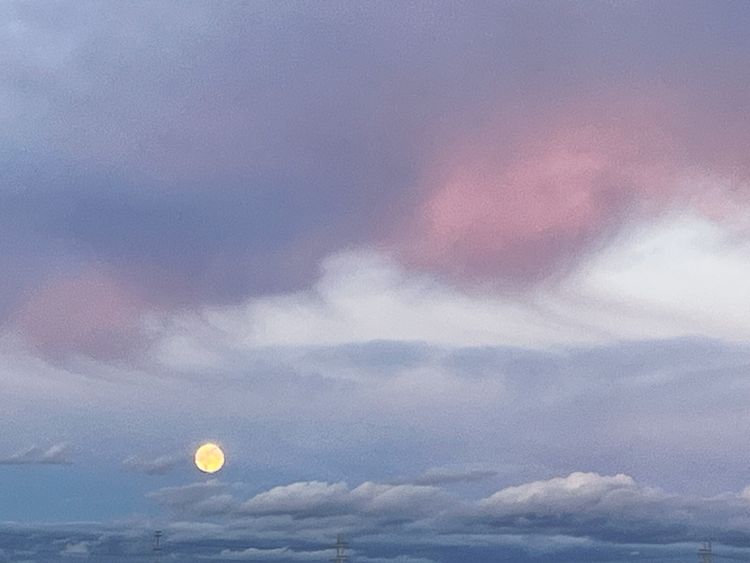 photo of the moon against a gray/blue/pink sky with a few clouds