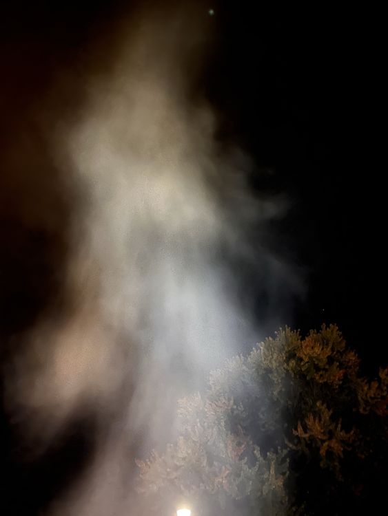 photo of smoke billowing up into the sky, with a tree and electric light in the background